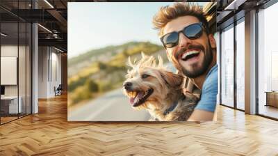 Smiling man wearing sunglasses, with his dog by his side, both leaning out of a car window at sunny day , seaside view Wall mural