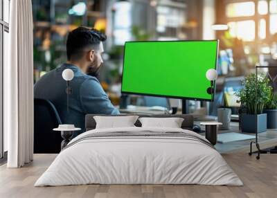 Young professional working at a desk with a green screen monitor Wall mural