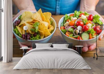 A hand holds a bowl of fresh vegetable salad while another hand holds a bowl of chips, symbolizing the choice between healthy and unhealthy food options Wall mural