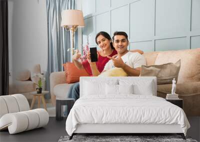 Happy Asian Indian young couple using smartphone at home while sitting on sofa or couch Wall mural