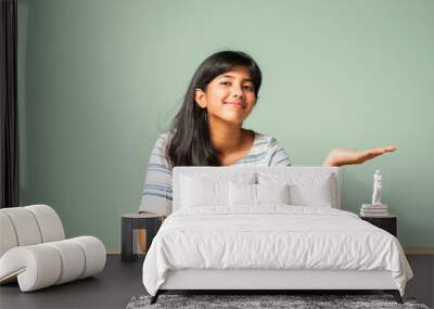 Happy Indian asian teenage girl showing or pointing something sitting at table Wall mural