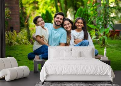 Happy Indian family of four sitting in park, embracing and smiling at camera, enjoying quality time Wall mural