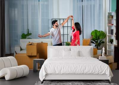 Happy Indian young couple dancing in modern living room with cardboard boxes with belongings. Wall mural