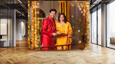 Indian couple celebrating Diwali at home by arranging diyas on balcony for traditional holiday joy Wall mural