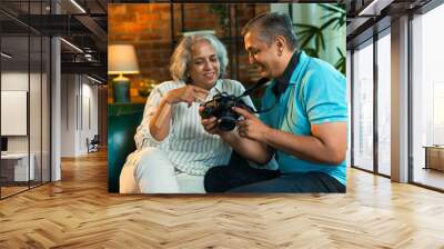 Indian couple in their fifties share laughter on the sofa while looking at photos on a DSLR Wall mural