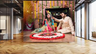 Indian couple making flower Rangoli on Diwali or Onam Festival, taking selfie or holding sweets Wall mural