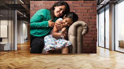 Indian mother and daughter on sofa, cuddling, tickling, selective focus Wall mural