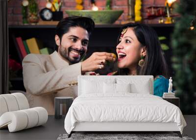 Indian smart couple eating sweet laddu on Diwali or anniversary, selective focus Wall mural