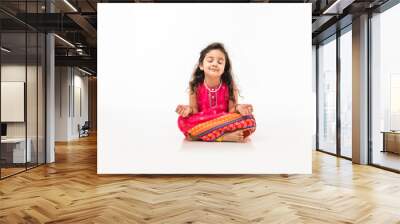 Portrait of cute little Indian girl model practicing and posing for pranayama or meditation while sitting isolated over white background with eyes closed Wall mural