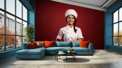 Pretty Indian female young Chef smiling and looking at camera while standing isolated on plain background Wall mural