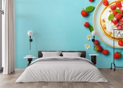 A top view of a plate with pancakes topped with whipped cream strawberries mint and sweet cherries on a bright blue background Ample copy space available Wall mural