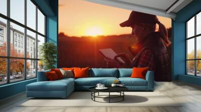 A female farmer is working in the field at sunset, enjoying a tablet. Technologies in agrobusiness Wall mural