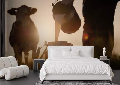 Farmer pours milk into can at sunset, in the background of a meadow with a cow Wall mural