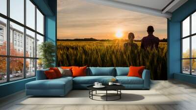 Two farmers, a man and a woman, are looking forward to the sunset over a field of wheat. Teamwork in agribusiness Wall mural