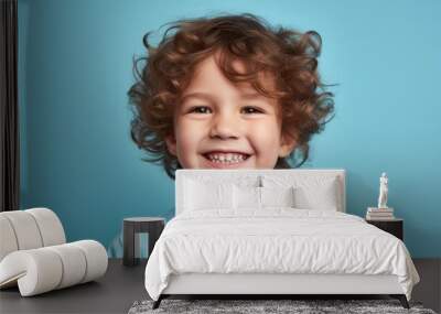 Portrait of a smiling little boy with curly hair on a blue background Wall mural