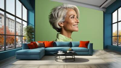 Portrait of smiling senior woman looking away over green background. Copy space. Wall mural