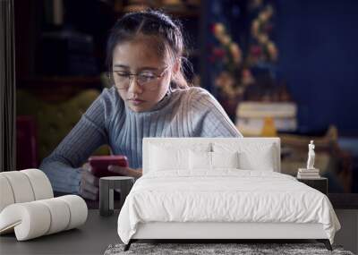 face of asian teenager reading message on smart phone in home living room Wall mural