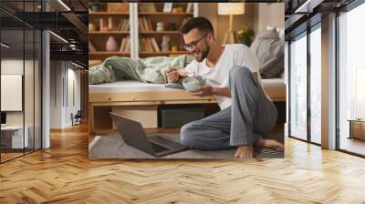 Young man with laptop having breakfast in bedroom Wall mural