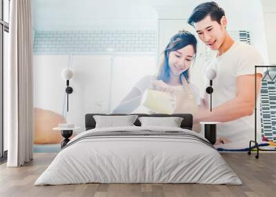 Asian couples cooking and baking cake together in kitchen room. Wall mural