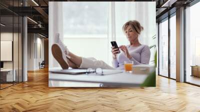 Mature woman relaxing and using her smartphone Wall mural