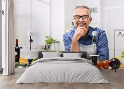 Smiling man posing in the kitchen, he is preparing healthy homemade food using fresh organic vegetables Wall mural