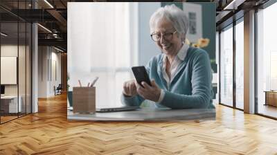 Smiling senior lady using her smartphone Wall mural