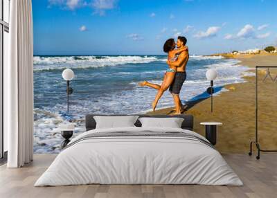 Happy young couple in bikini and shorts enjoying summer at the beach at dusk, breathing fresh air, kissing and teasing one another Wall mural