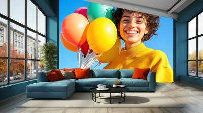 A joyful person holding colorful balloons against a bright blue sky, radiating happiness and positivity. Wall mural