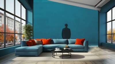 A solitary figure in all-black, facing a vast blue wall, conveying themes of isolation and contemplation in modern life. Wall mural