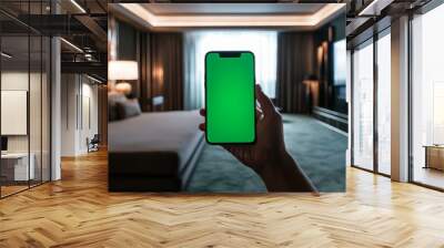 Hand holding smartphone with green screen in modern bedroom, ideal for tech or lifestyle themes. Wall mural