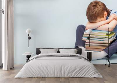 Upset schoolboy sitting with pile of school books and covers his face with hands. boy sleeping on a stack of textbooks Wall mural