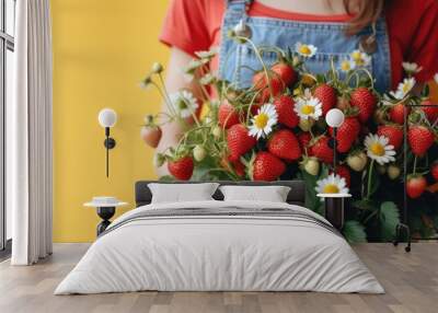 Woman holding a bouquet of strawberries with flowers chamomile on yellow studio background Wall mural