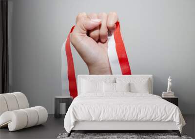 A woman's hand holds a red and white ribbon as a symbol of the Indonesian flag. Isolated on white background Wall mural