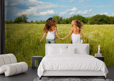 Two happy young women running on green field under blue sky Wall mural