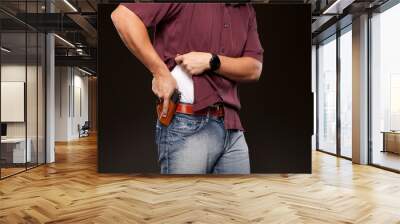 Man lifting up his shirt about to draw his concealed carry pistol from his holster. Wall mural