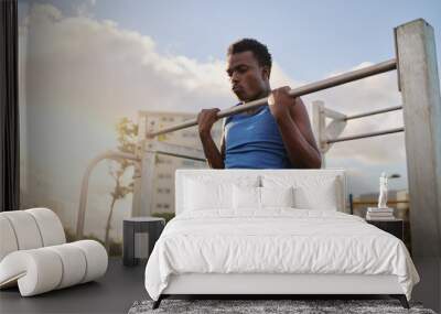 An african american young fit man doing pull ups on horizontal bar in the public park outdoors Wall mural