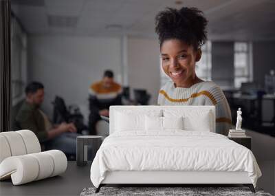 Cheerful young african american businesswoman in casual wear holding digital tablet smiling and looking to camera while her colleagues communicating in the background - female entrepreneur - women Wall mural