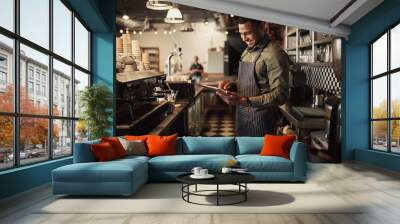 Cheerful young afro-american cafe owner wearing black striped apron using digital tablet Wall mural