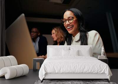 Close-up of successful smiling young African American businesswoman sitting near coworkers using laptop in office Wall mural