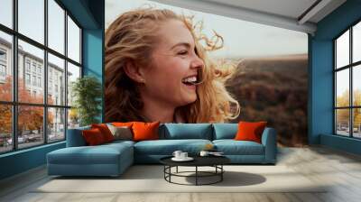 Closeup of a laughing young woman enjoying windy breeze touching face with hair flying while looking away - the feeling of freedom in nature Wall mural