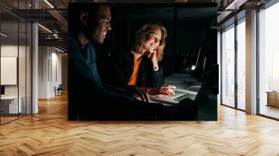 Diverse creative business people working with laptop overtime at night in low light at office Wall mural