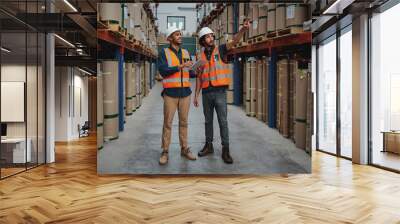 Full length of joyful professional managers working together while being in the warehouse holding digital tablet pointing towards cardboard box on shelf Wall mural