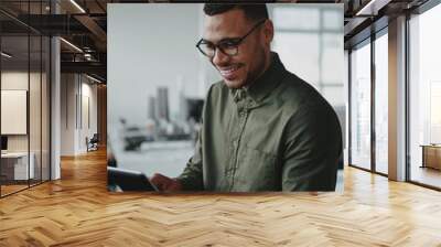 Handsome young african american businessman sitting in office smiling while using a smartphone Wall mural