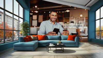 Happy african man holding mobile phone typing card data to make online payment sitting in cafe Wall mural