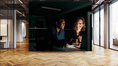 Happy businessman and businesswoman working on laptop overtime in night time Wall mural