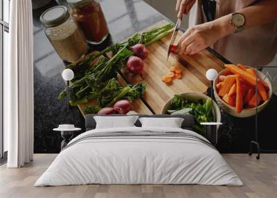 High-angle closeup of young female hands chopping fresh orange carrot on board while in modern kitchen Wall mural