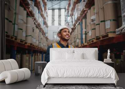 Low angle view of young african man wearing reflective jacket holding digital tablet standing in factory warehouse smiling Wall mural