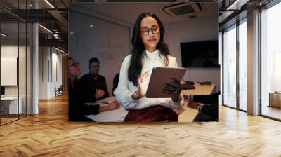 Portrait of a businesswoman using digital tablet with her team sitting at desk in meeting room Wall mural