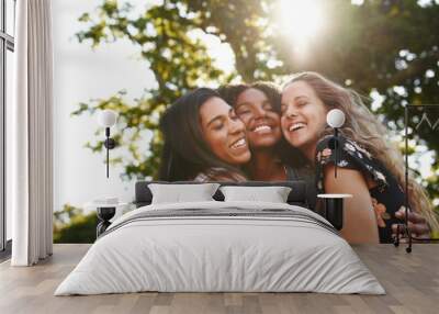 Portrait of a happy multiethnic group female friends hugging and embracing each other laughing and having fun outdoors in a park  Wall mural