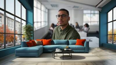 Portrait of a serious young professional businessman wearing eyeglasses looking at camera while colleague at background Wall mural